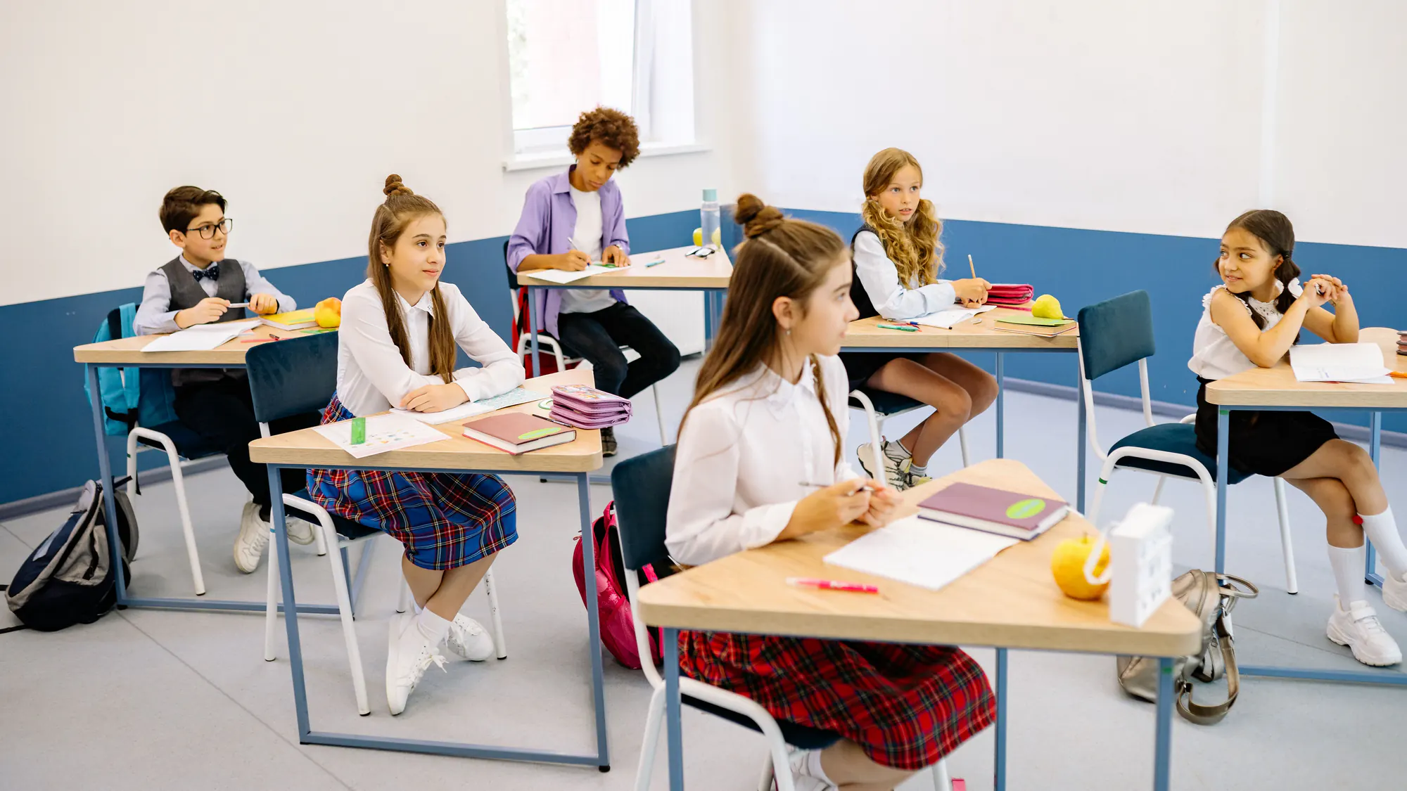 Élèves en uniforme assis à leur pupitre dans une salle de classe claire, attentifs au cours