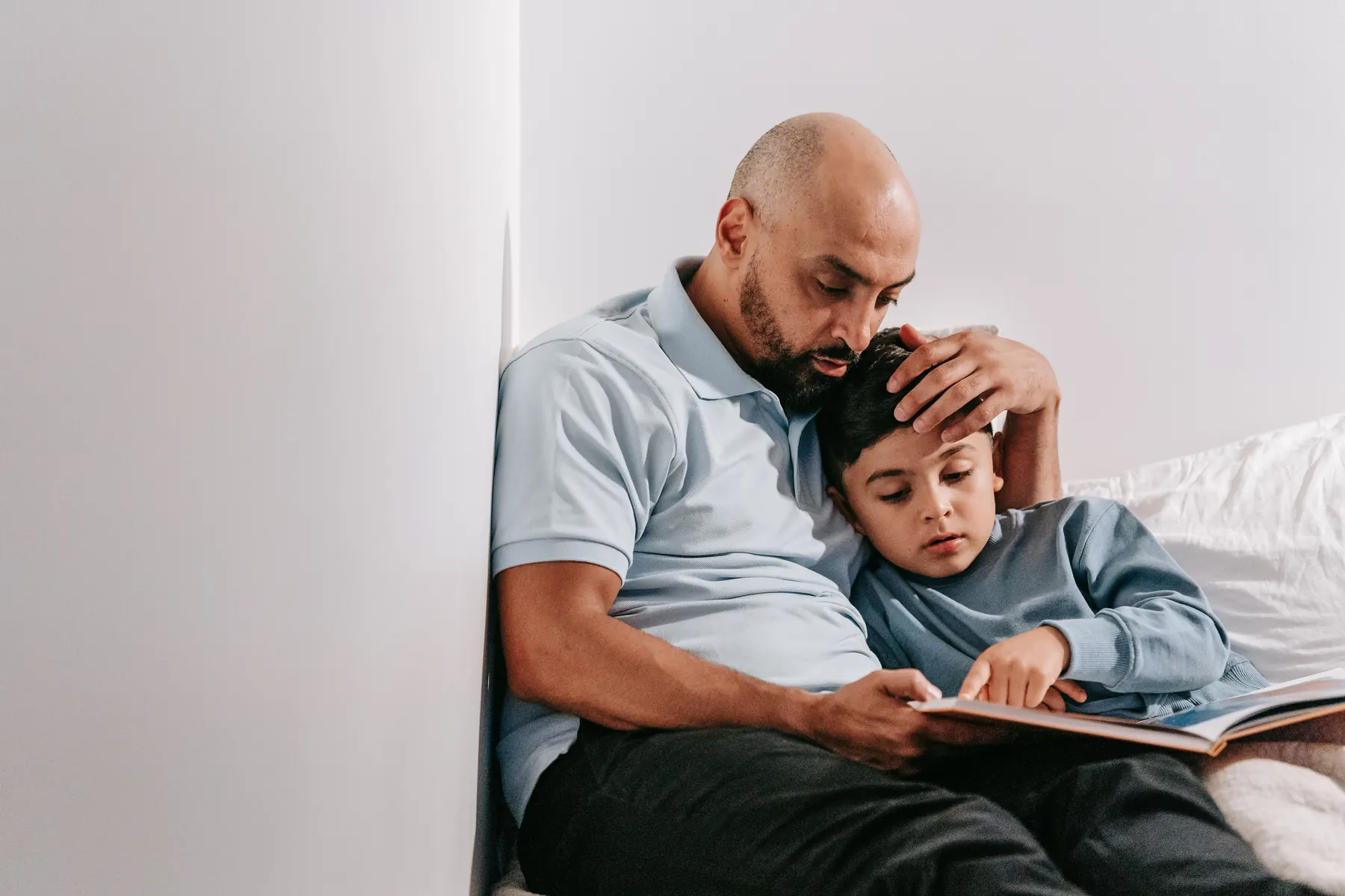 Un père lit un livre avec son jeune fils blotti contre lui, la main posée sur sa tête