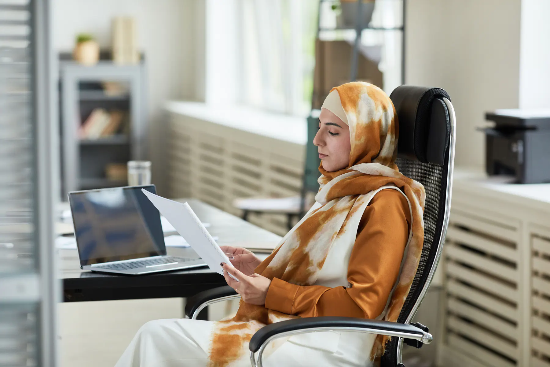 Une gestionnaire relit un document à son bureau, à côté de son ordinateur portable